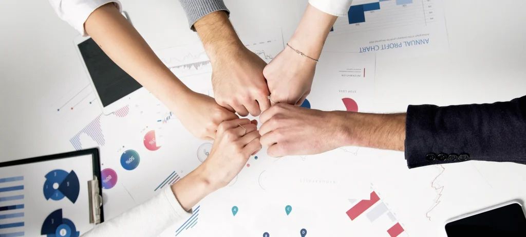 Team members bumping fists over data charts, symbolizing unity and alignment.