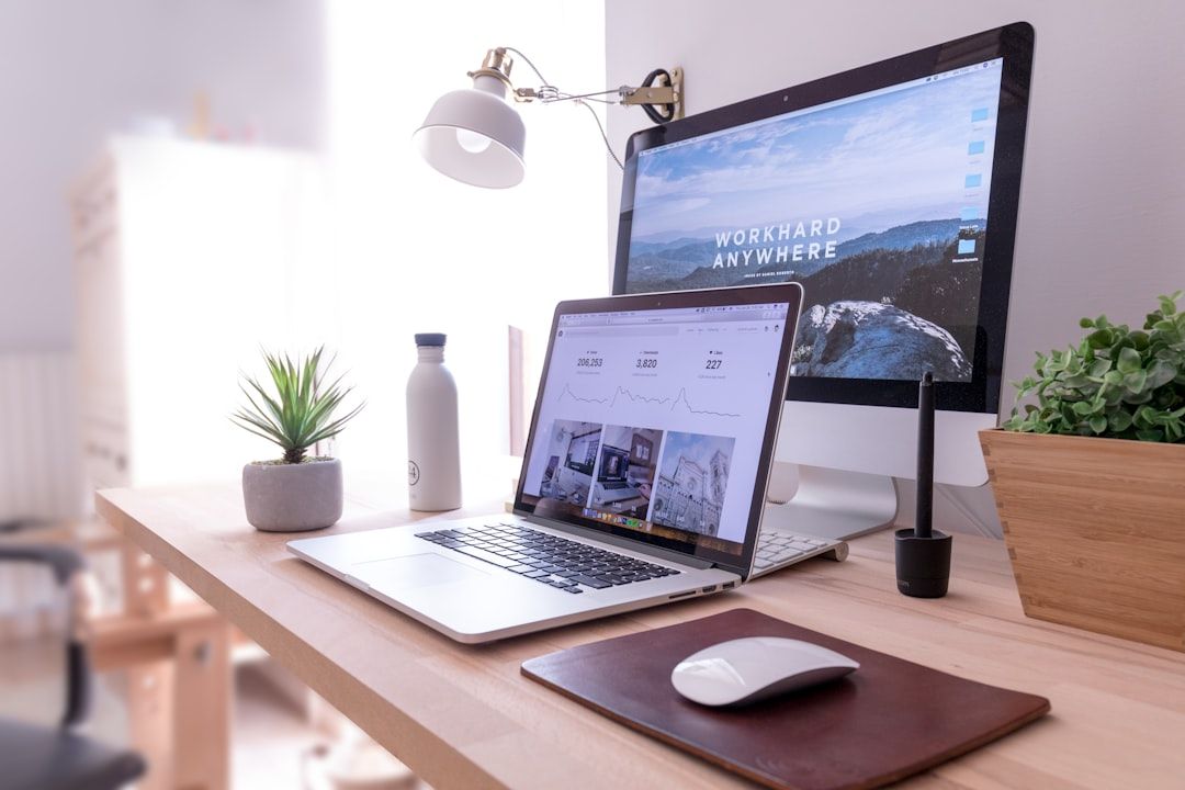 A modern digital workplace setup with a laptop, desktop monitor, and mouse on a wooden desk.