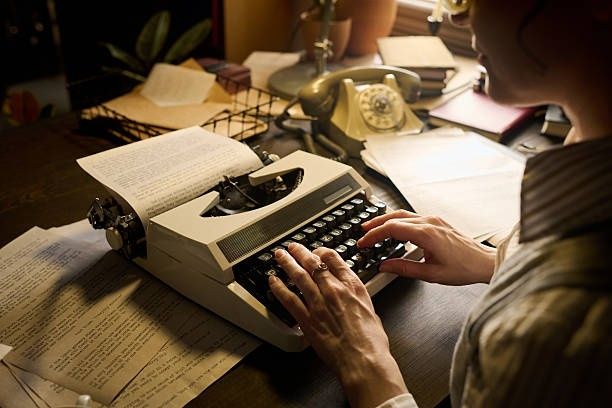 Hands typing a manuscript on a vintage typewriter beside marked pages